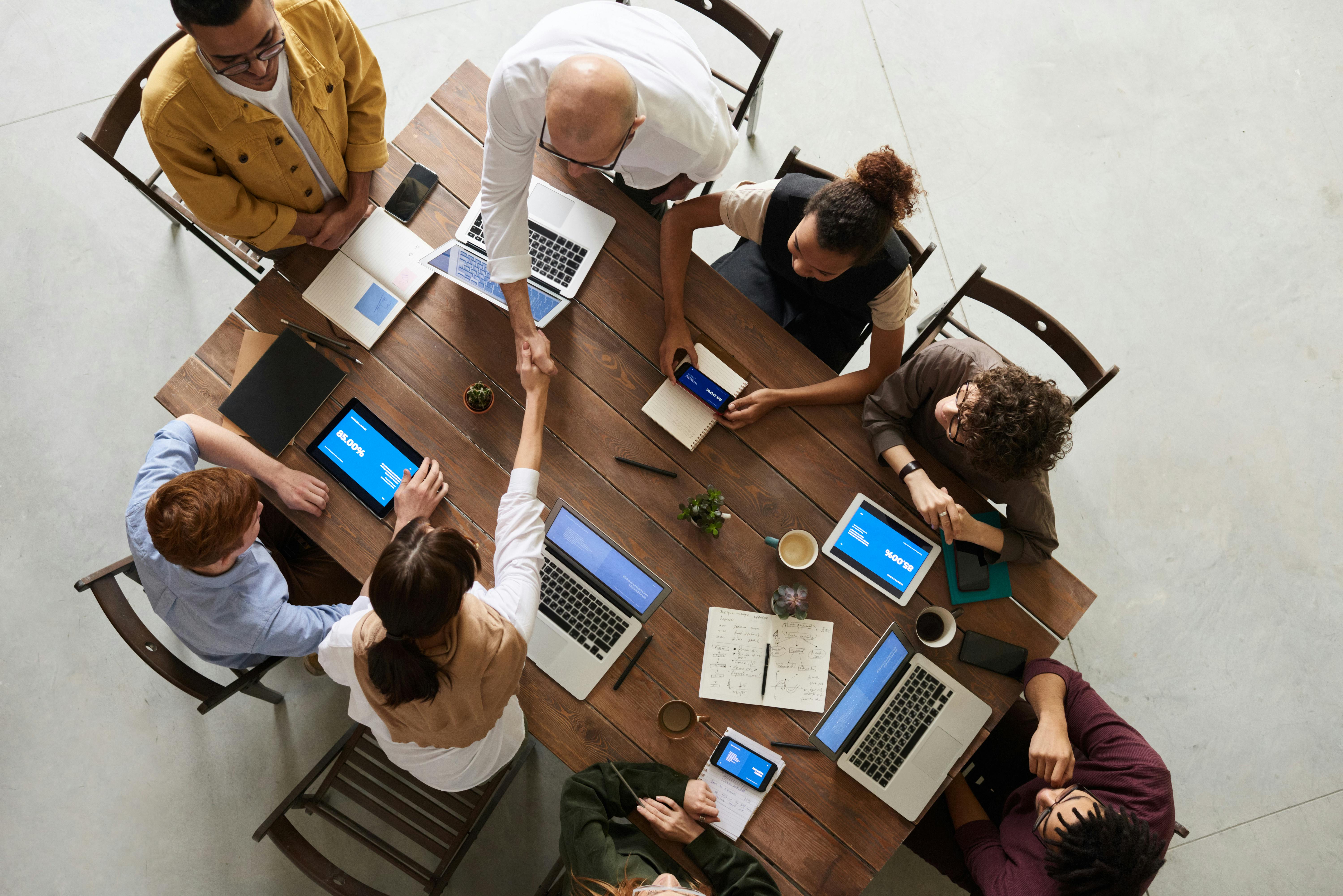 Corporate setting, people working together at a desk, two of them shaking hands
